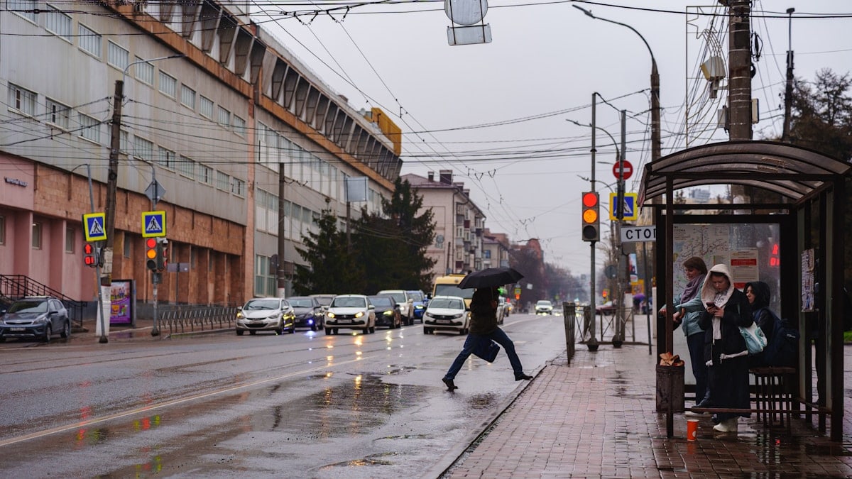 Pedestrian crosses street on rainy day at bus stop